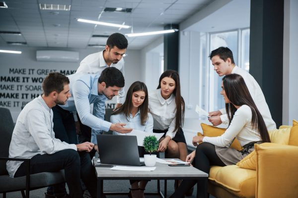 Guy shows document to a girl. Group of young freelancers in the office have conversation and working.